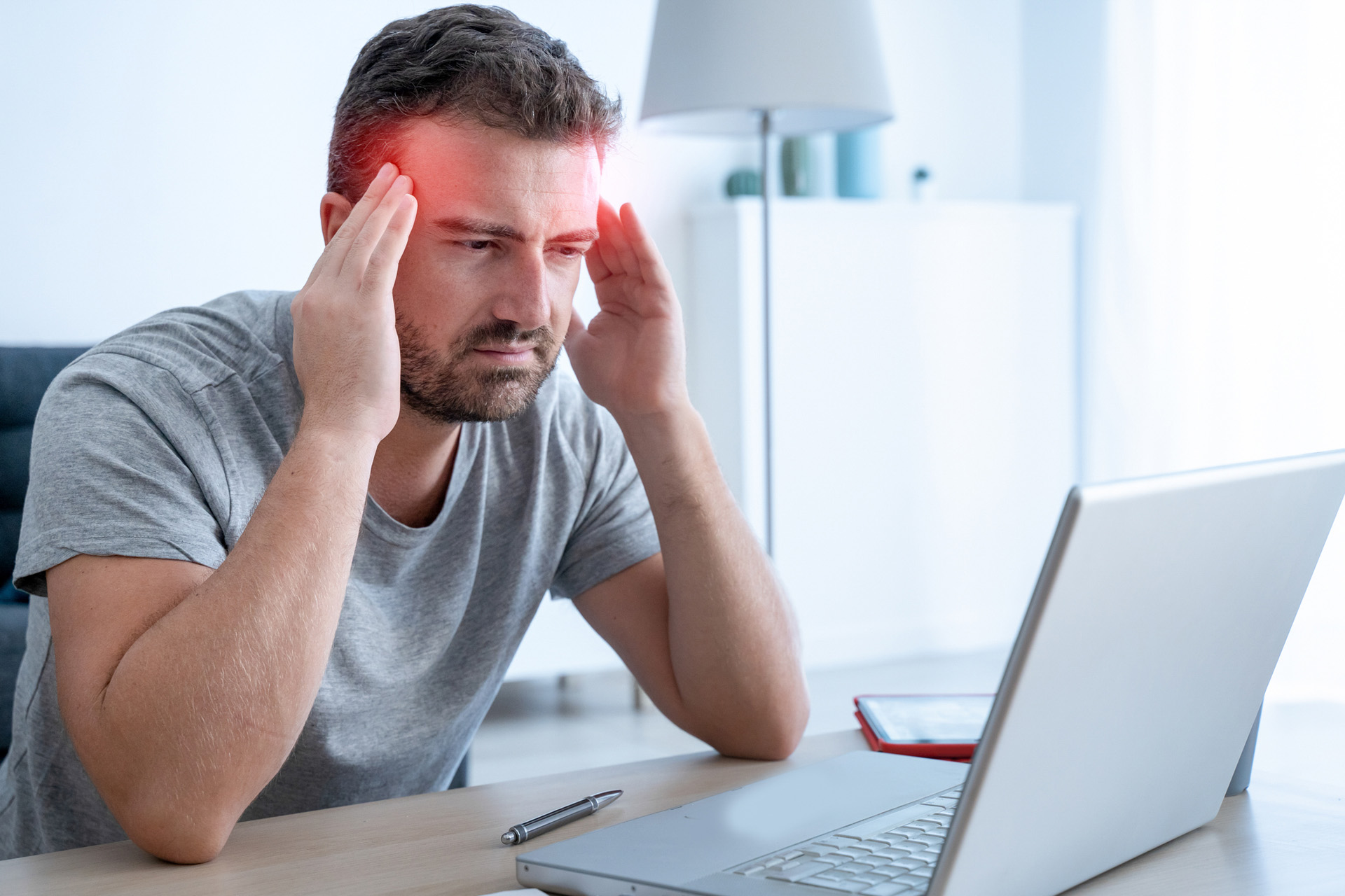 Mann mittleren Alters mit Migräne reibt sich die Schläfen vor dem Laptop.